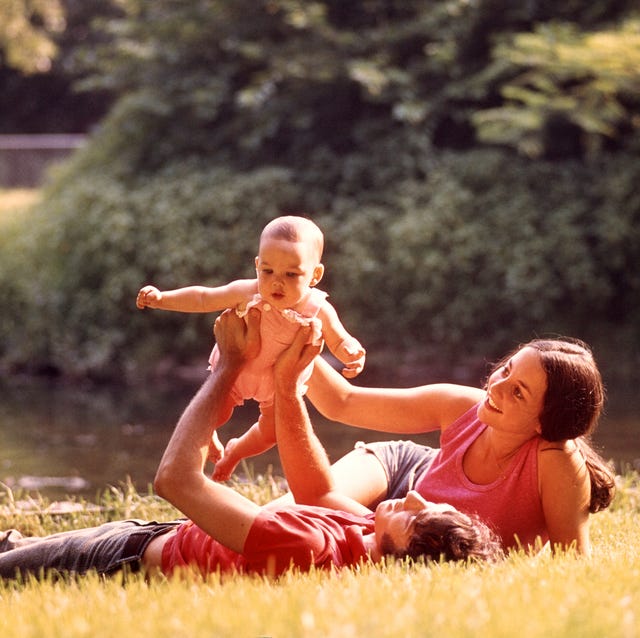 1970s COUPLE LYING IN... 1970s couple lying in grass holding baby up above father (photo by photo media/classicstock/getty images)