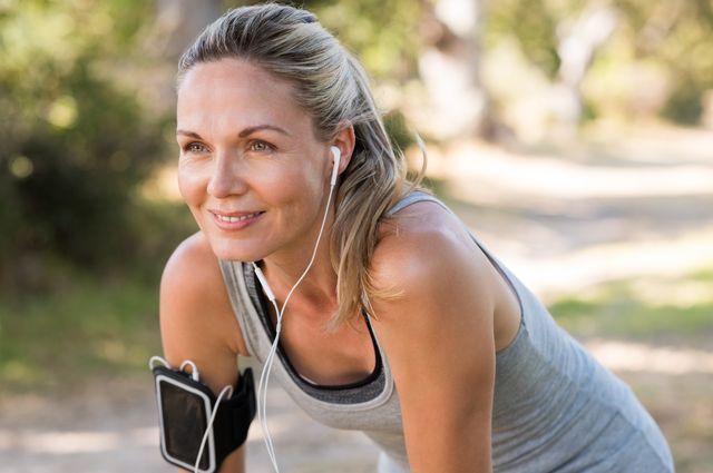 portrait of athletic mature woman resting after jogging beautiful senior blonde woman running at the park on a sunny day female runner listening to music while jogging