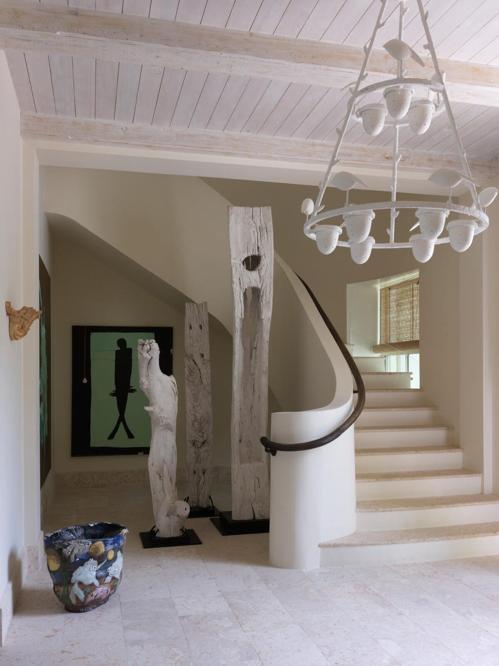 Photograph of entryway with staircase, including ceramic bowl and wooden sculptures.