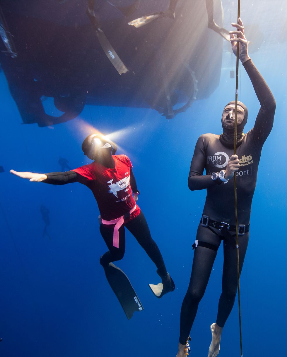 underwater image of divers, in wet suits, with eqipment, next to boat