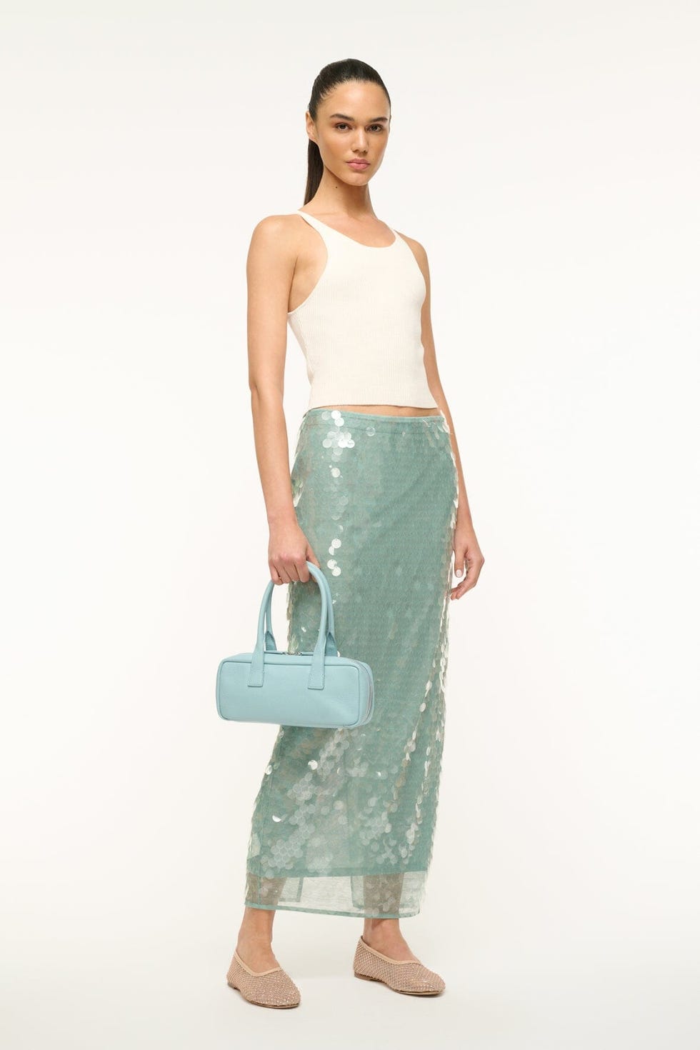 a model showcases a stylish outfit featuring a cropped tank top and a shimmering sequin skirt complemented by a blue handbag