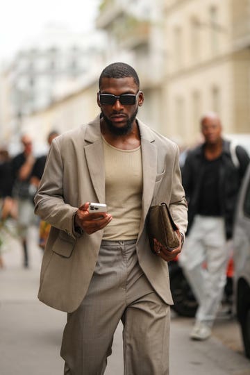 a man wearing sunglasses and a brown jacket holding a cell phone