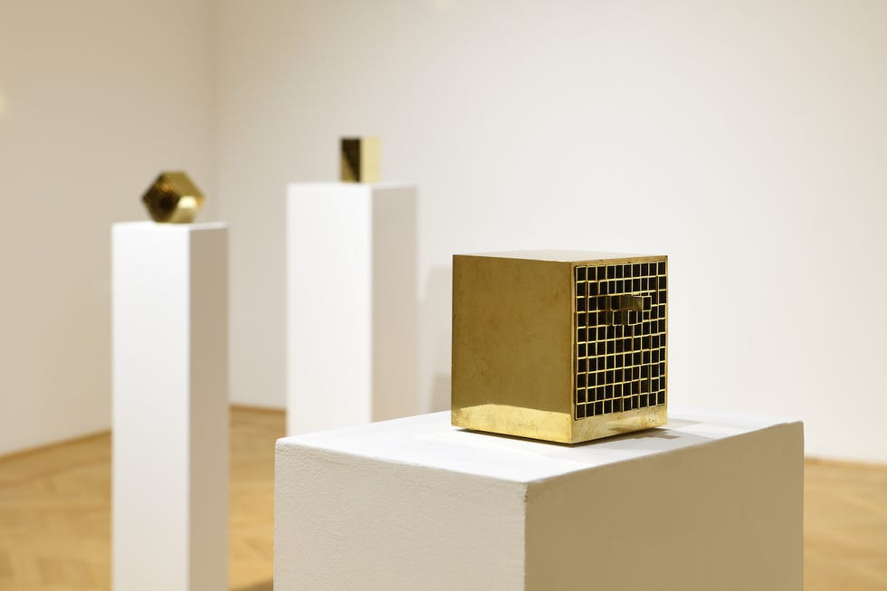 three geometric sculptures displayed on pedestals in a gallery