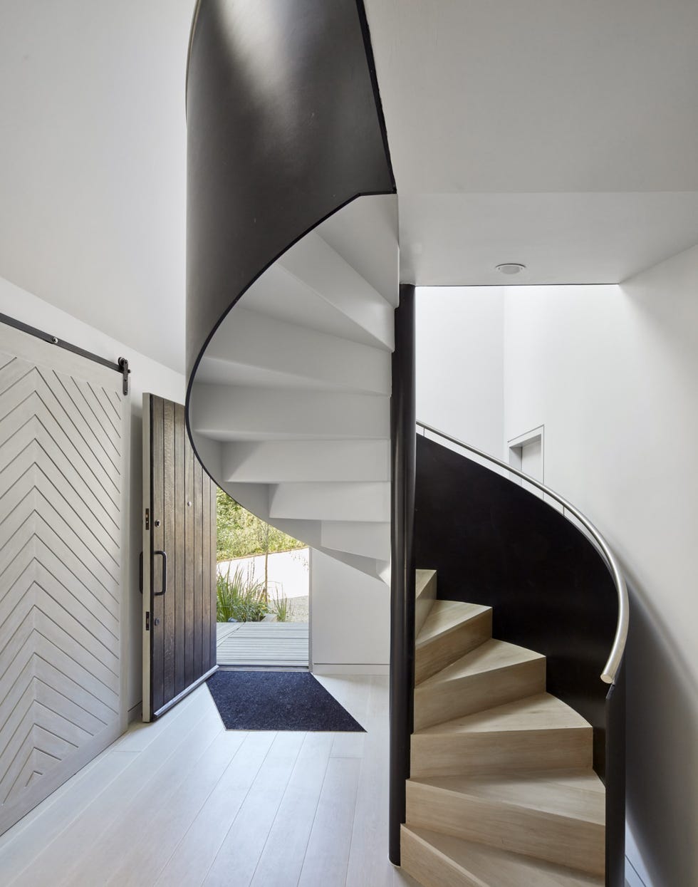 a white hallway with a tall black spiral staircase