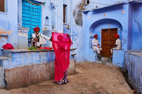 In Jodhpur Rajasthan contrasteert de karmijnrodedupattasjaal van een vrouw met de pastelkleurige muren van de blauwe stad