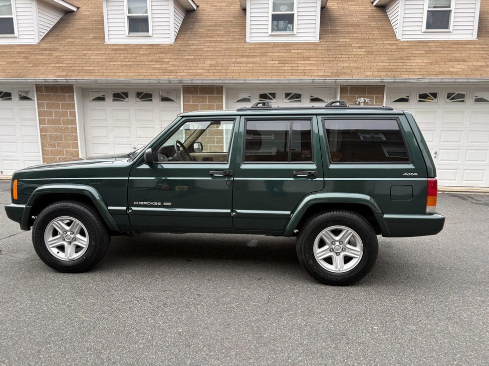 side profile of a green jeep cherokee 4x4 with silver alloy wheels, parked in front of a residential garage.
