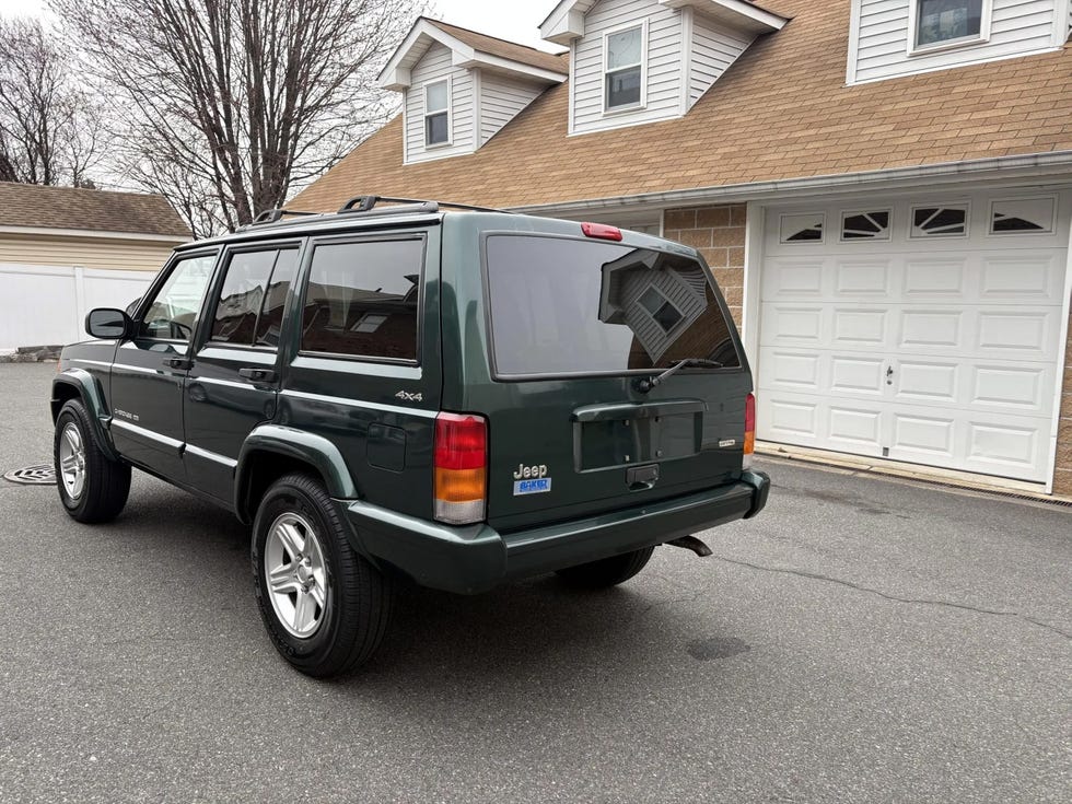 rear three quarter view of a green jeep cherokee 4x4, showcasing its tailgate, roof rails, and silver alloy wheels.