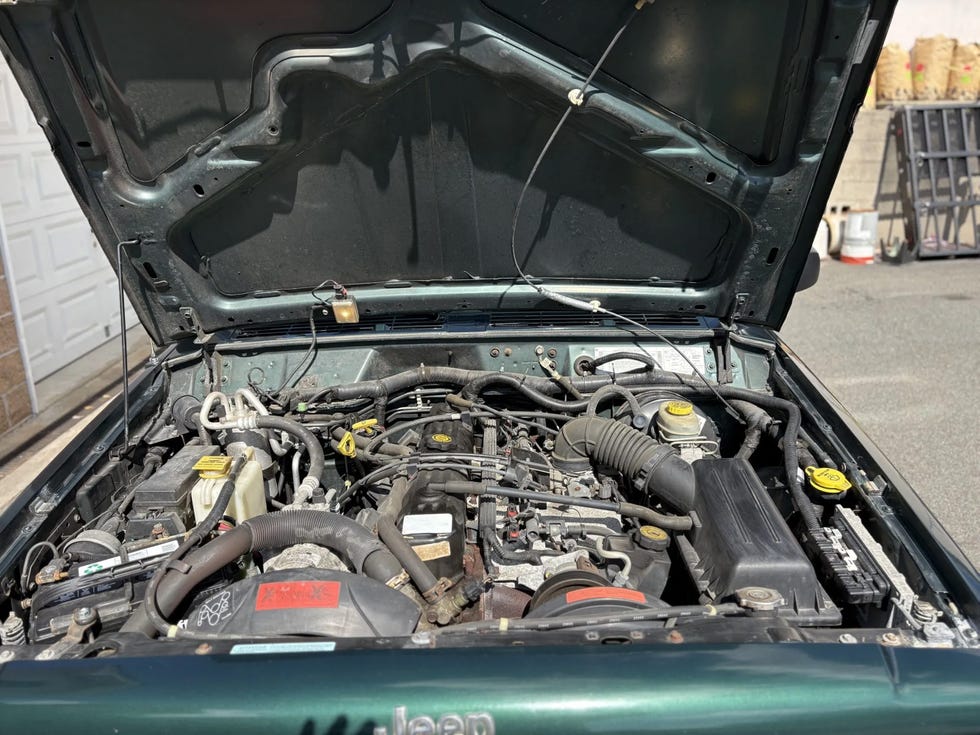 engine bay of a jeep cherokee, showing various components, hoses, and wiring under the hood.