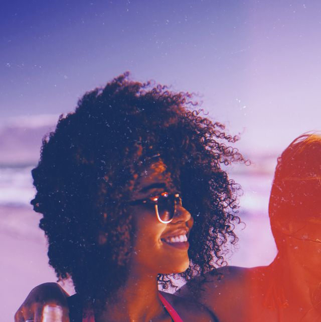 smiling afro girl walking happily with her friend on a windy beach carrying alcopops