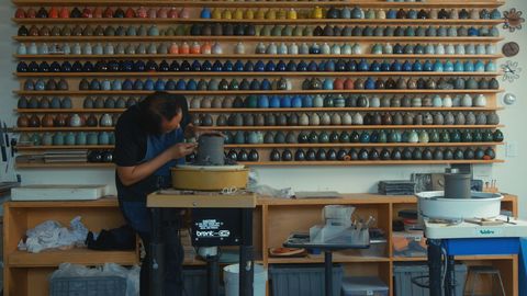 potter at wheel in front of colorful ceramics