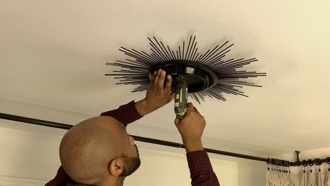 man drilling mirror into ceiling