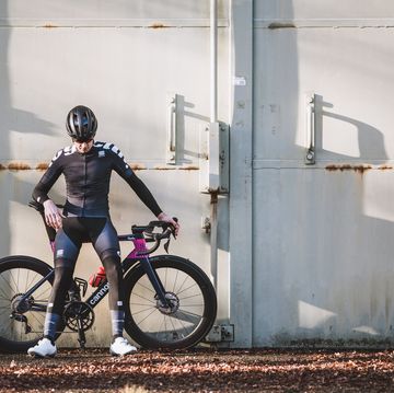 wielrenner in fietskleding inclusief beenstukken en armstukken staand met racefiets