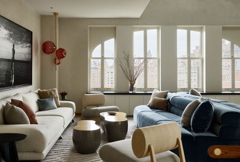 living area with tall arched windows and facing sofas in cream and in blue velvet with a striated cream rug and sinewy curved coffee tables and a round back chair and a red blown glass light fixture standing in the far left corner