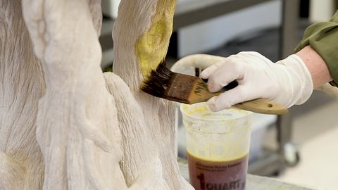 medium closeup image of a gloved hand applying acid stain to a sculpture layered with fiber cement