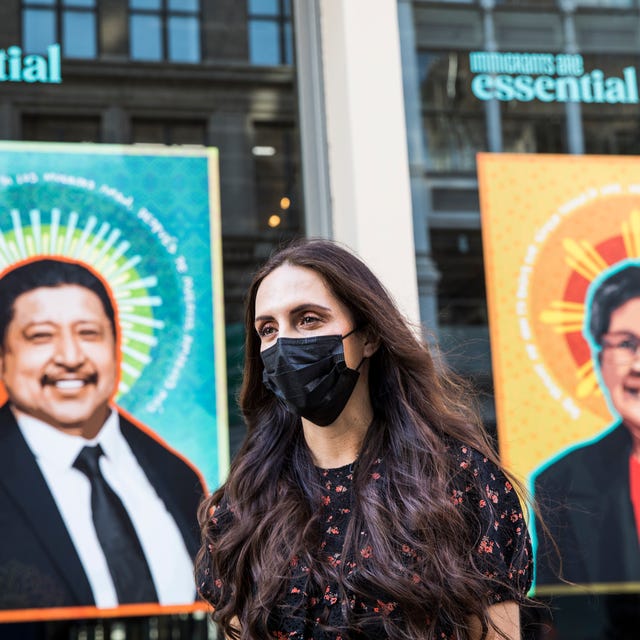 paola stands in front of two portraits from the art installation wearing a black face mask