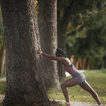 black woman leaning up against a tree as she stretches her legs