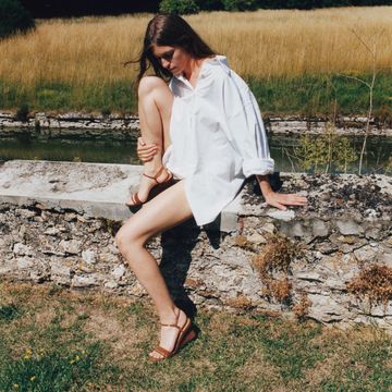 a model wears a pair of wedge sandals on a stone wall in a field