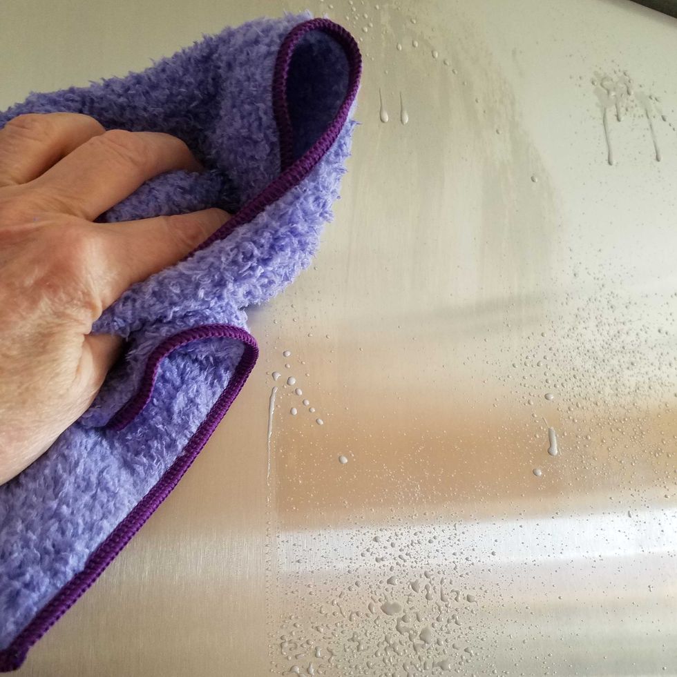 purple microfiber cloth wiping cleaner off stainless steel appliance