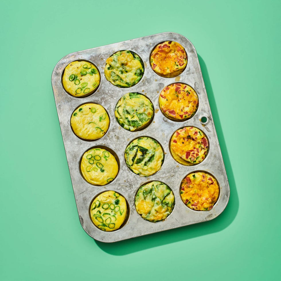 a metal muffin pan of twelve baked egg muffins, on a green background