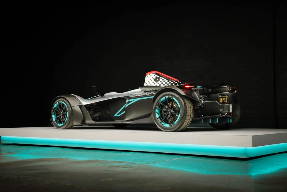 rear three quarter view of a single seater sports car with a checkered roll hoop, turquoise accents, and exposed rear suspension.