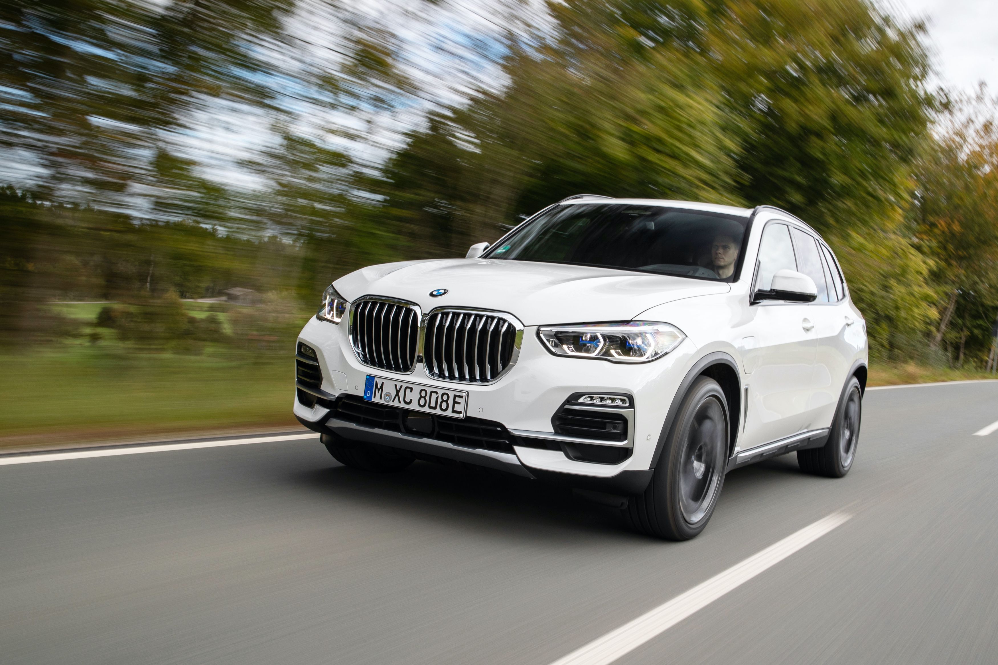 2023 white bmw x5 suv driving along tree lined road