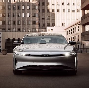a silver 2023 lucid air touring sedan parked face front in a city yard with tall buildings in the background