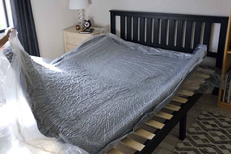 a compressed mattress in plastic unrolled on a bed frame