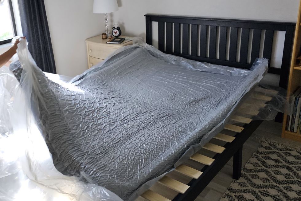 a compressed mattress in plastic unrolled on a bed frame