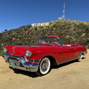 a red car parked on a dirt road with hollywood sign in the background