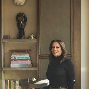 a woman standing next to a shelf with books and a lamp