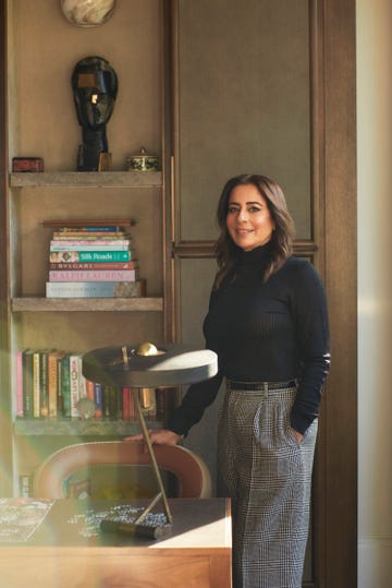 a woman standing next to a shelf with books and a lamp