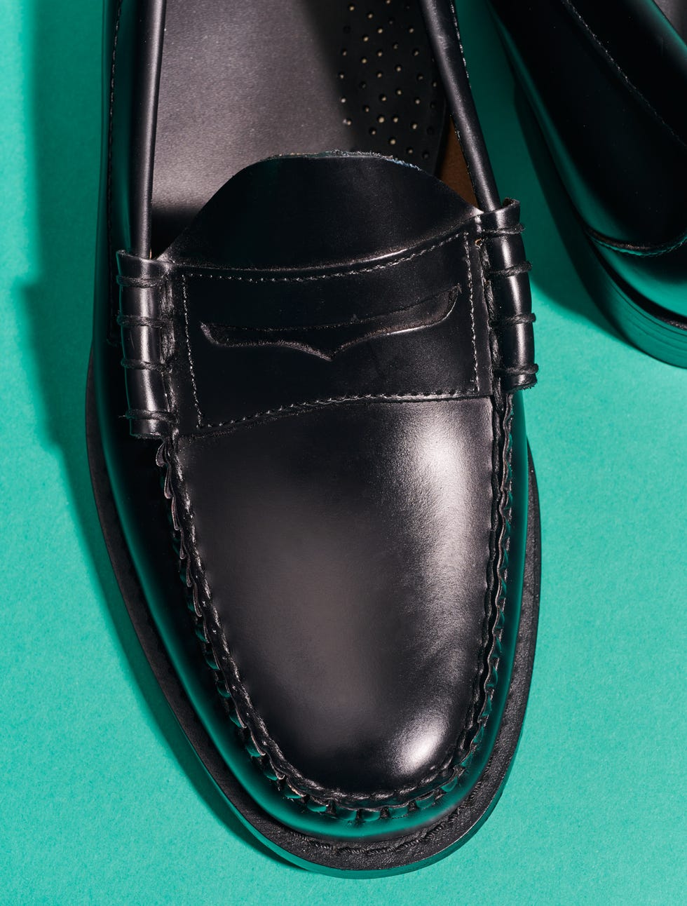 top view of a black leather loafer shoe with decorative stitching on a teal background