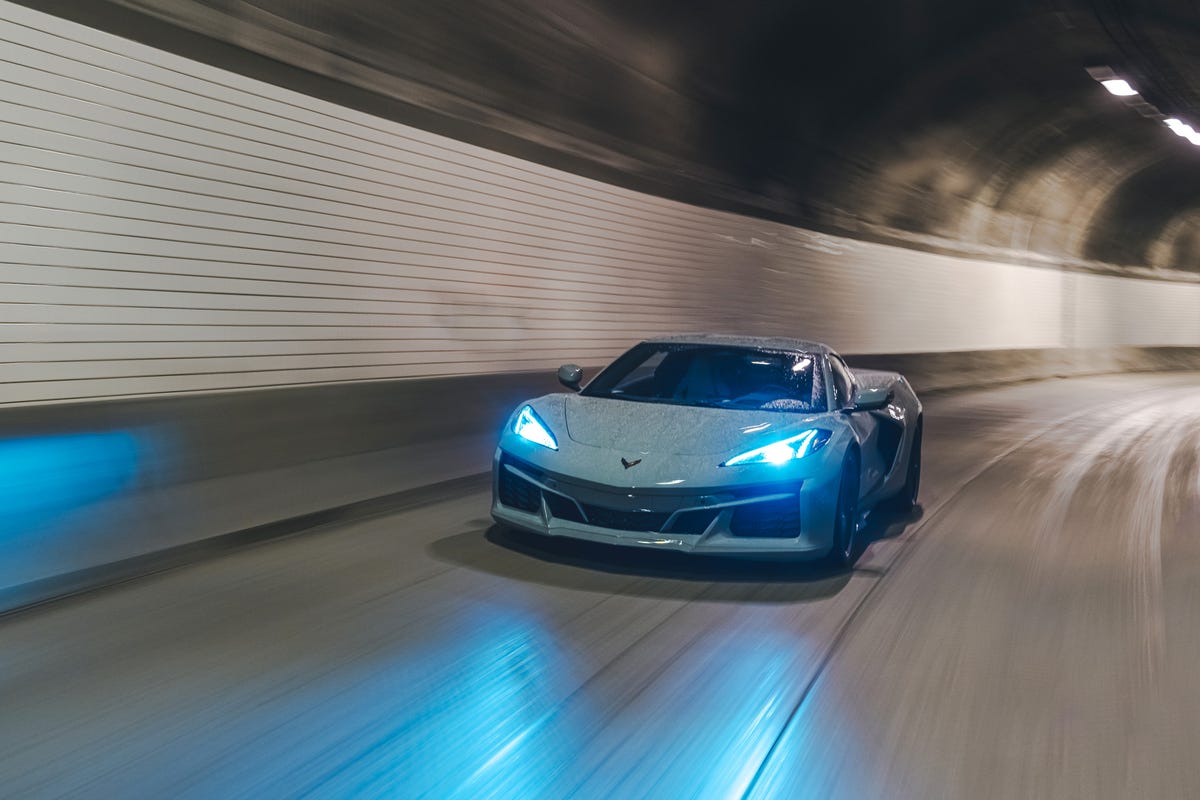 Vorderansicht eines hellgrauen Chevrolet Corvette E-Ray, der mit leuchtend blauen Scheinwerfern durch einen Tunnel fährt.