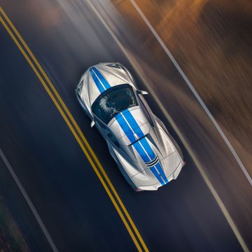 overhead view of 2024 chevrolet corvette e ray 3lz convertible in silver flare with electric blue stripe package driving on a road pre production model shown actual production model may vary model year 2024 corvette e ray available 2023