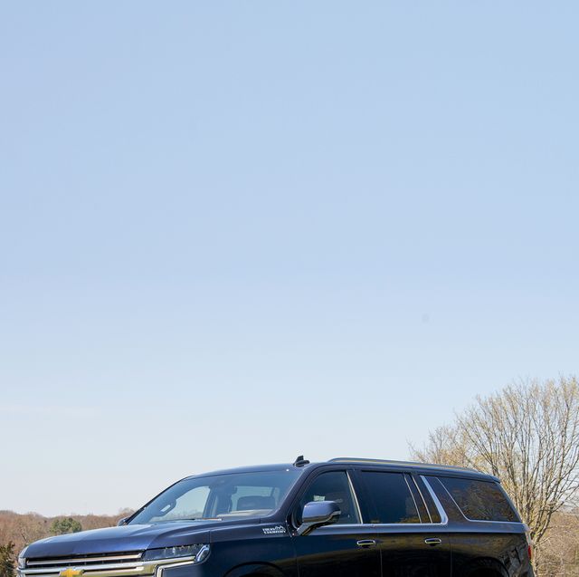 a dark blue four door chevy suburban suv is parked in a field facing the camera