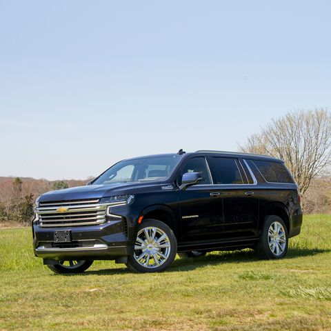 a dark blue four door chevy suburban suv is parked in a field facing the camera