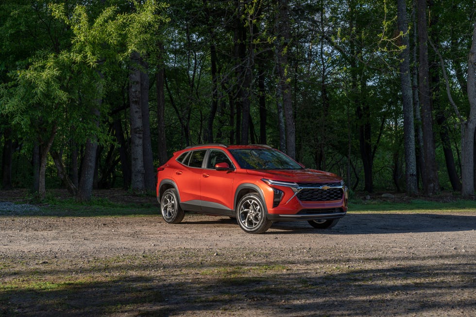 front 34 view of 2024 chevrolet trax lt in cayenne orange metallic parked on a gravel road in front of trees