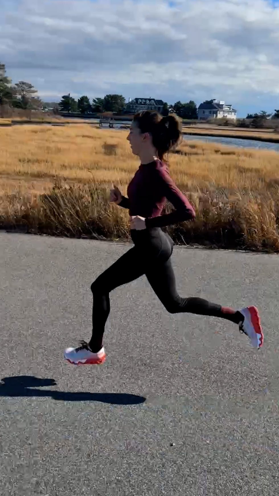 person running on a pathway near a marshy area with houses in the background