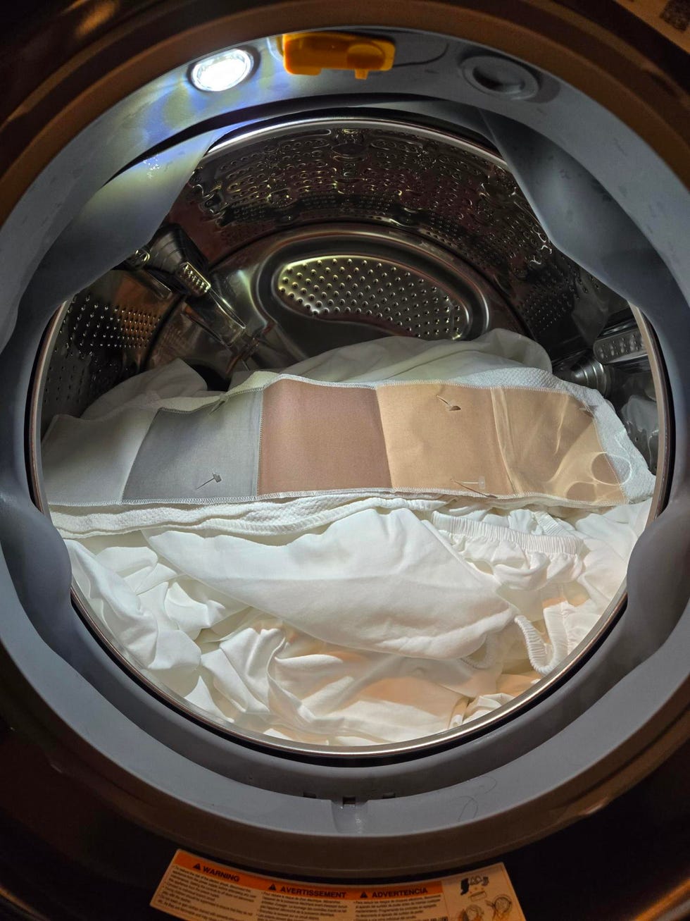 a stain swatch with 6 stains placed on a load of sheets in a front loading washing machine
