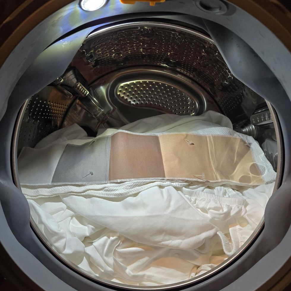 a stain swatch with 6 stains placed on a load of sheets in a front loading washing machine