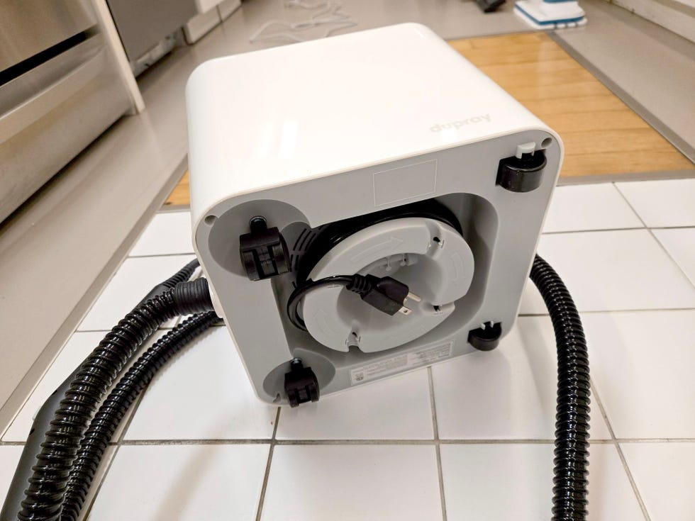 cord reel and wheels on the bottom of the dupray neat steam cleaner set on a tiled floor