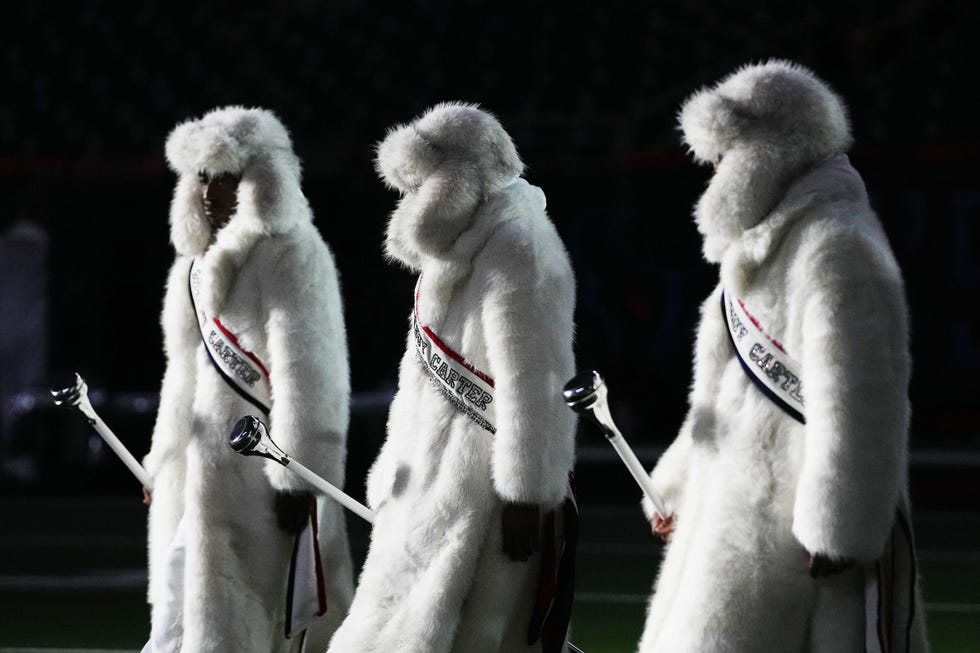 Three performers in white fur coats with sashes holding maces