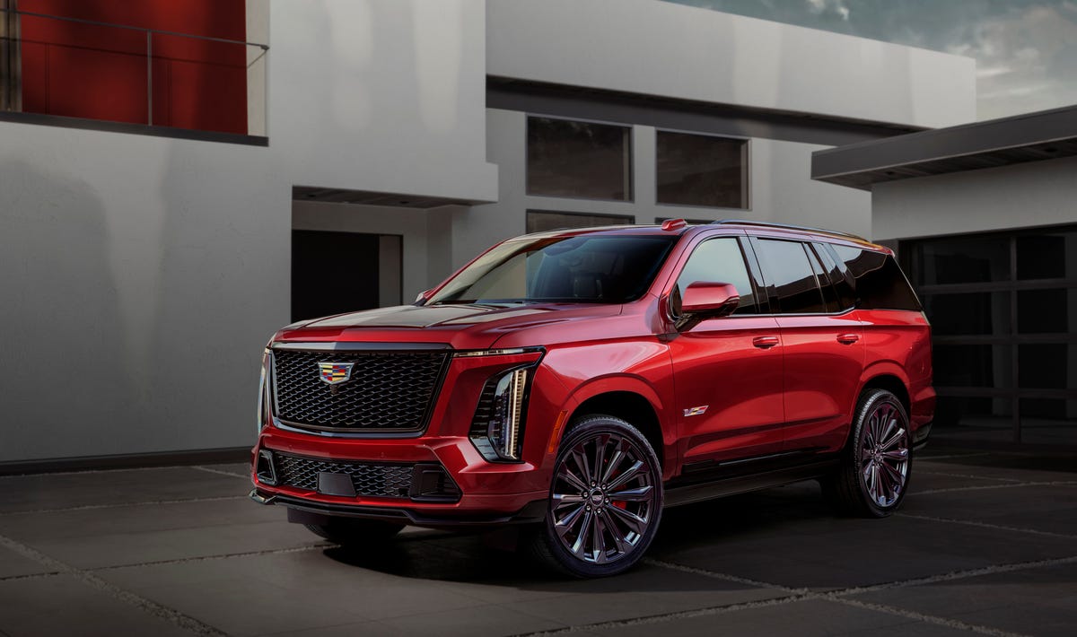 front side view of red suv with vertical led headlights, black grille, and multi spoke wheels parked in driveway.