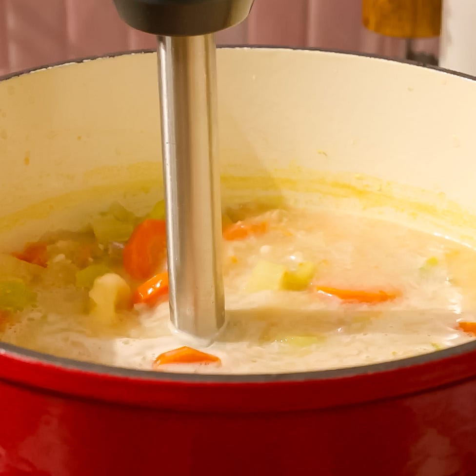 blender submerged in a pot of soup with vegetable chunks