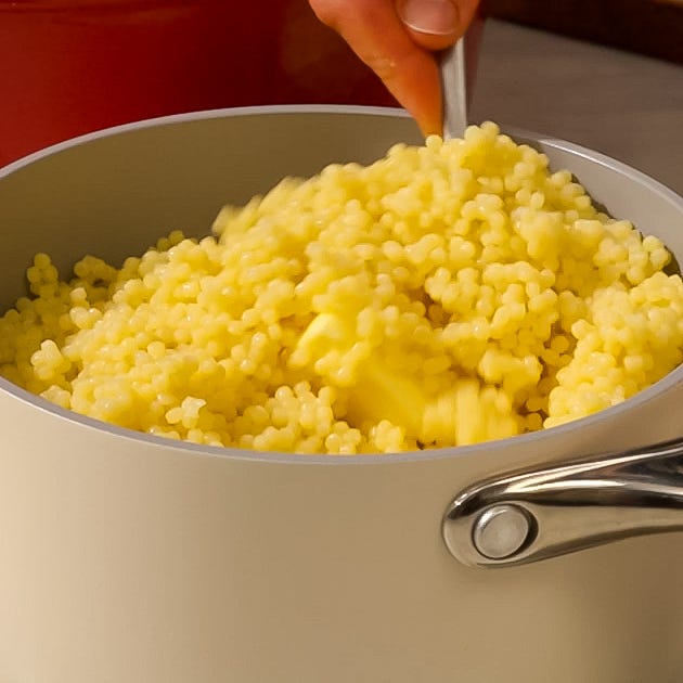 cooked couscous being mixed with butter in a pot