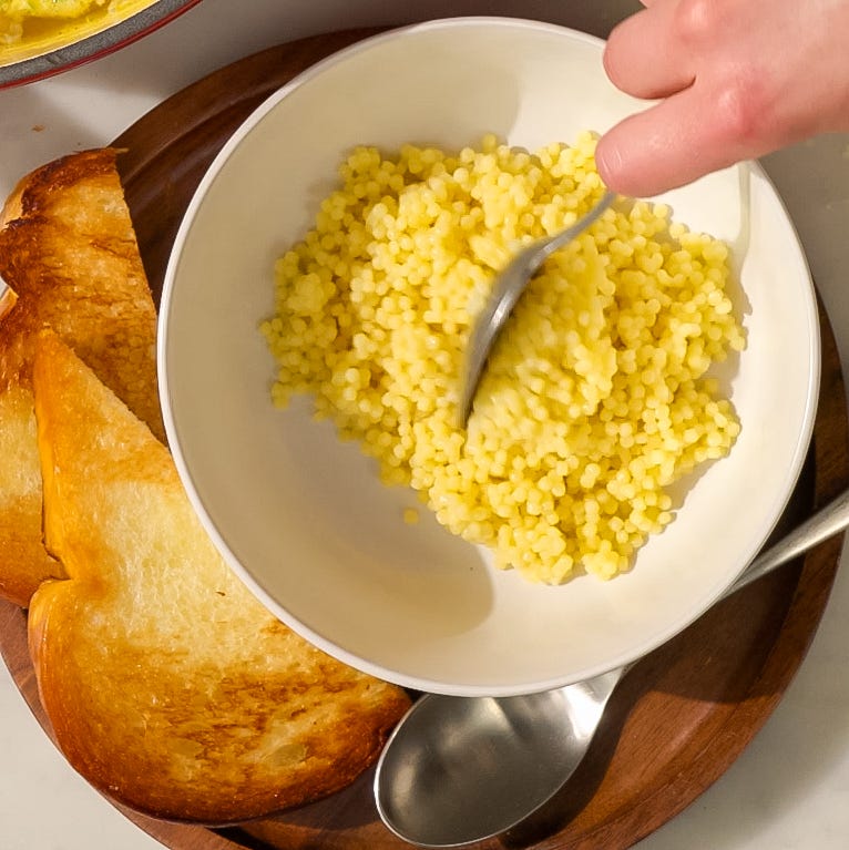 bowl of yellow couscous with slices of toasted bread on a wooden platter