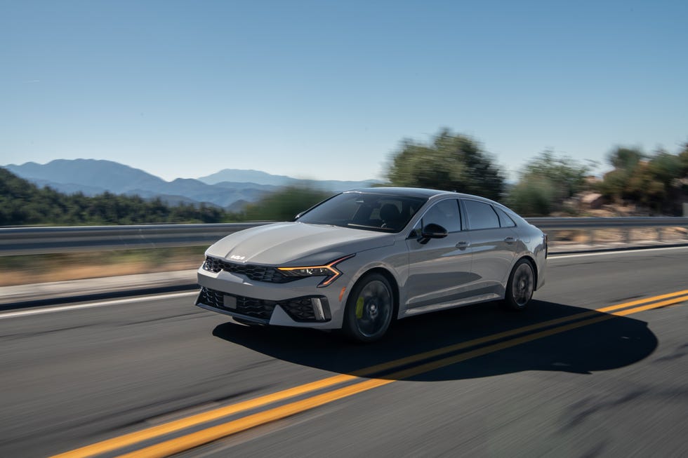 front three quarter view of a silver sedan in motion on a winding road with mountains in the background.