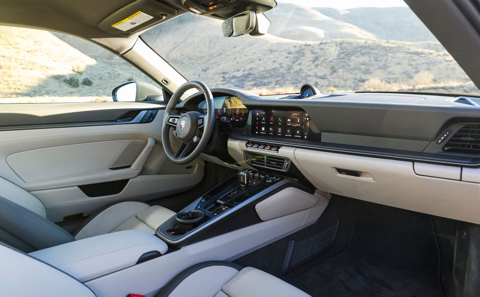 interior view of a car cabin featuring a digital dashboard, touchscreen display, and beige leather seats with a scenic background.