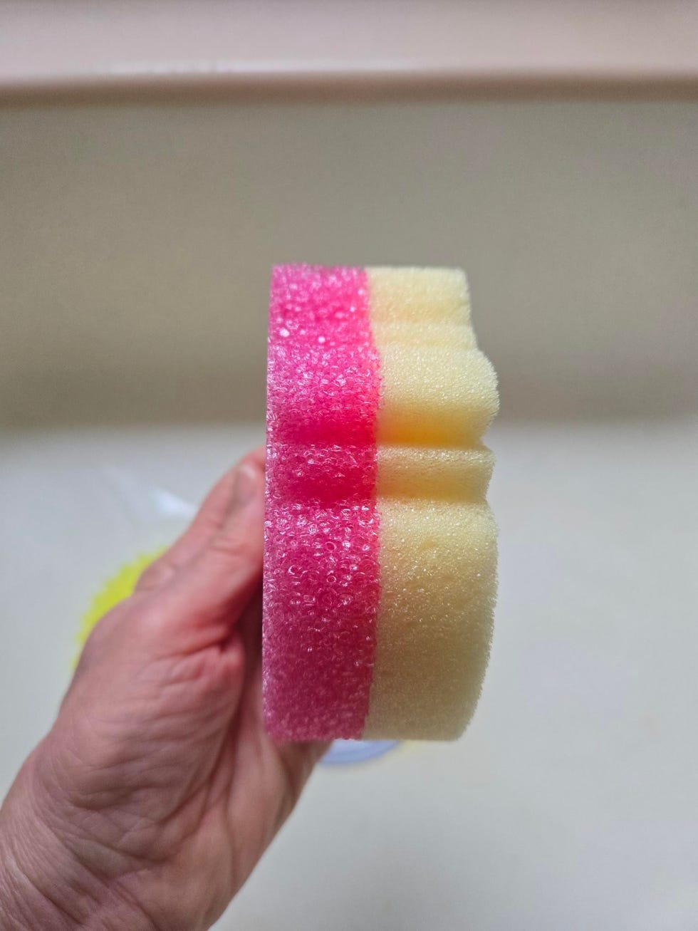 a hand holding a multicolored scrub mommy sponge with a pink and yellow layered design