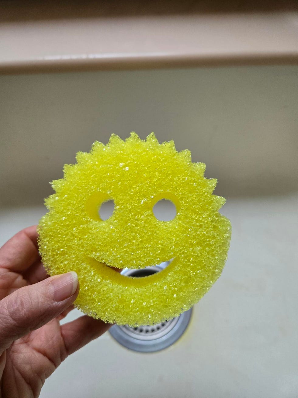 a yellow scrub daddy sponge shaped like a smiling face being held